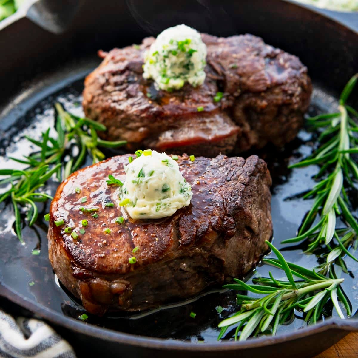 Square side shot of cast iron filet mignon with herb butter on top.