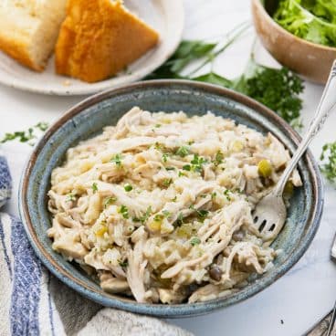 Square side shot of crockpot chicken and rice on a white table with cornbread and salad.
