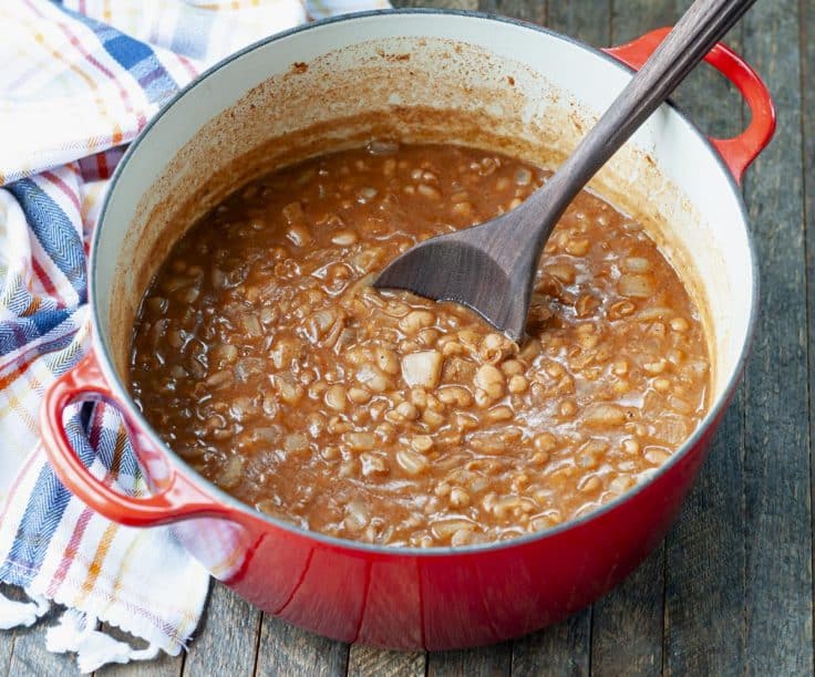 Horizontal shot of a wooden spoon stirring a Dutch oven full of ranch style beans.