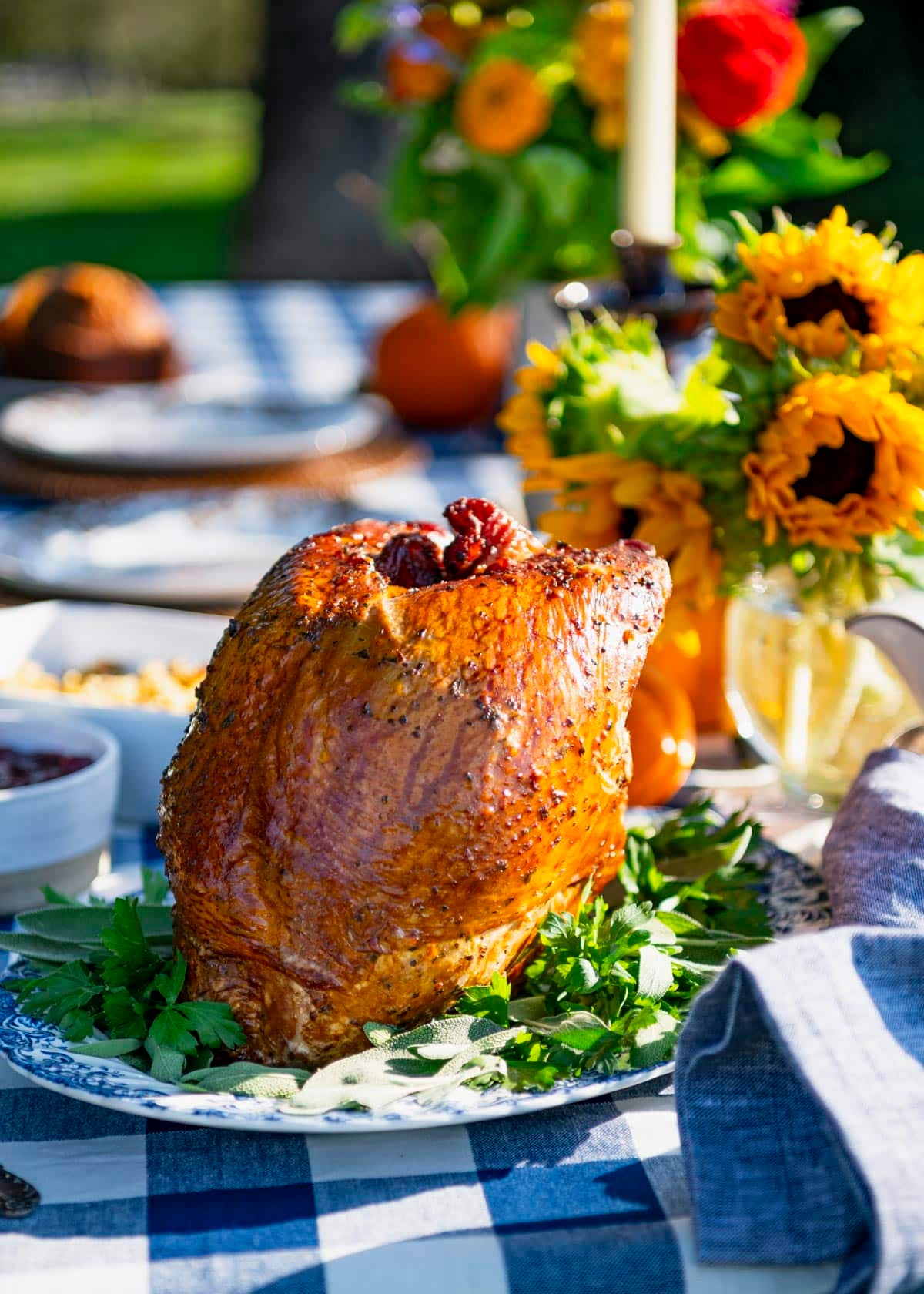 Side shot of a smoked turkey breast on a holiday table with fresh flowers and pumpkins.