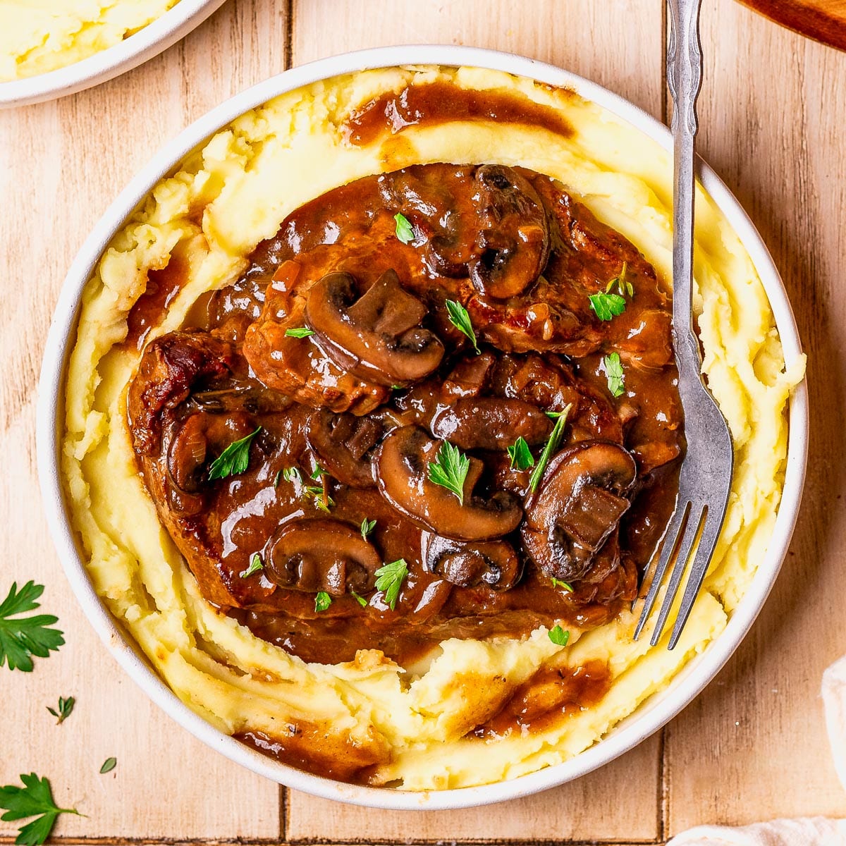 Square overhead shot of a bowl of smothered round steak with gravy on a bed of mashed potatoes.