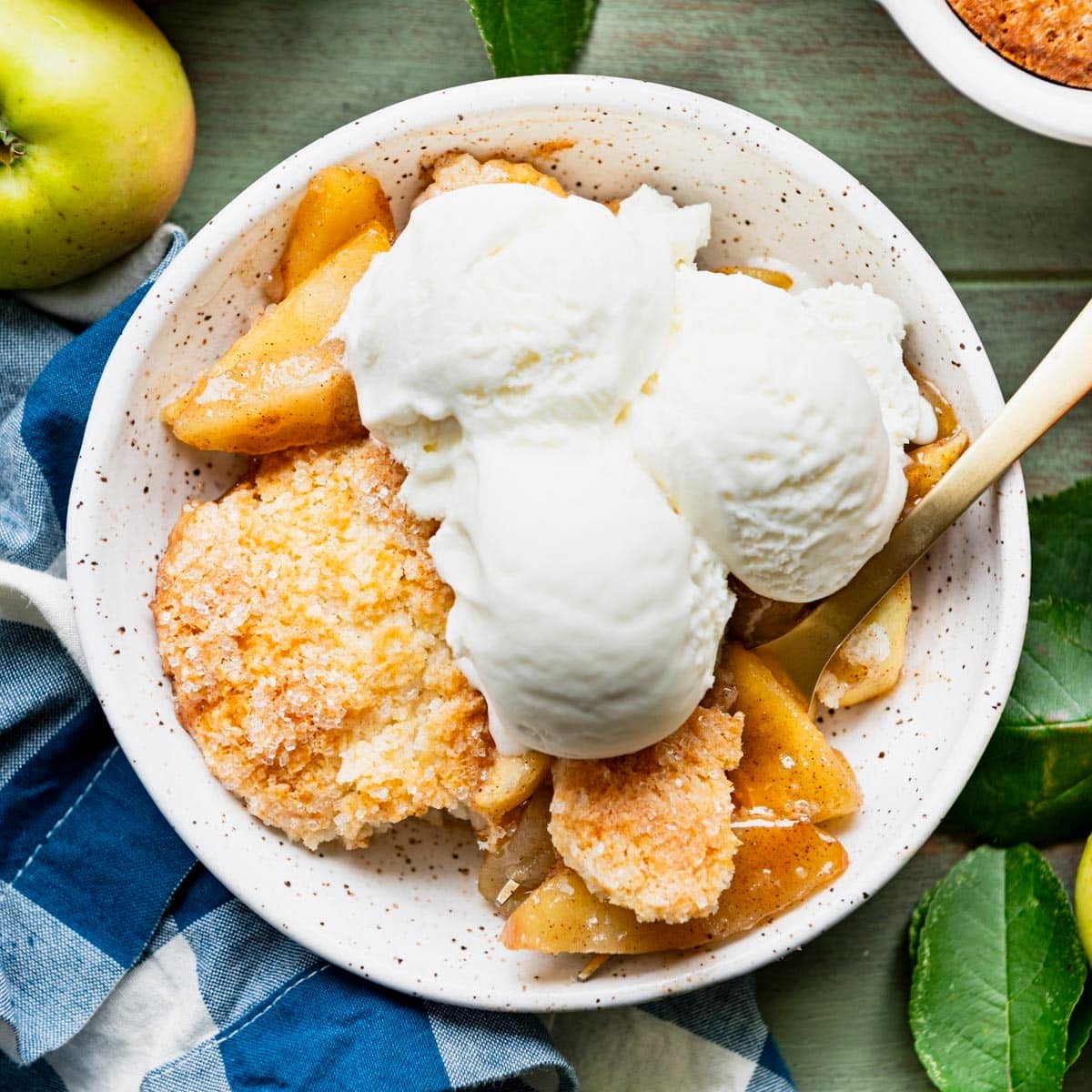 Square overhead shot of a white bowl full of traditional apple cobbler with scoops of vanilla ice cream on top.