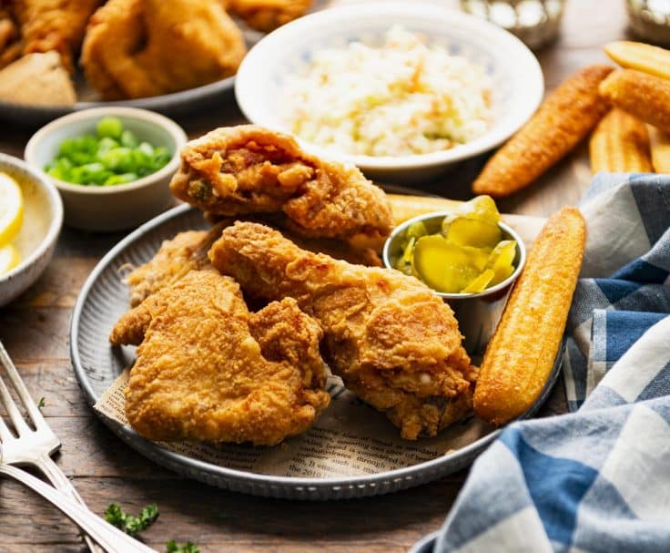 Horizontal front shot of the best Southern fried chicken recipe on a serving tray with coleslaw and cornbread in the background.