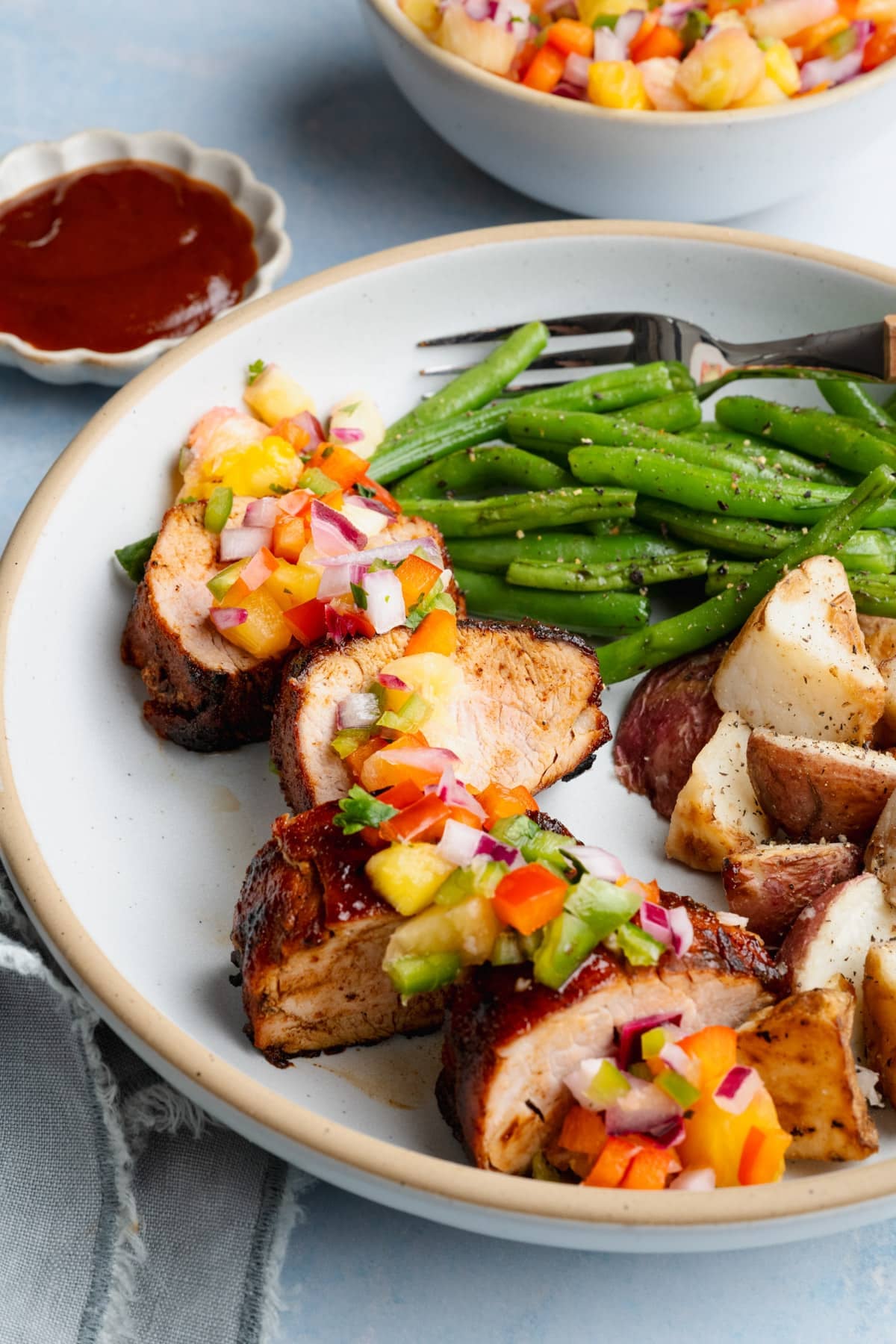 Side shot of a sliced grilled pork tenderloin on a plate with a fresh pineapple salsa garnish.
