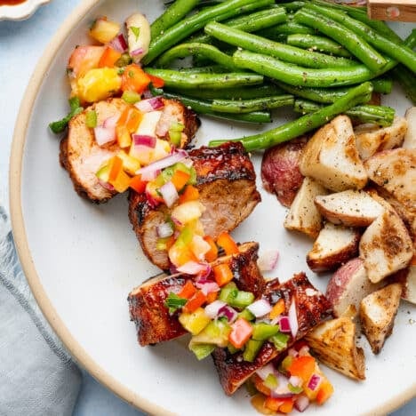 Square overhead shot of a sliced grilled pork tenderloin on a plate with a fresh pineapple salsa garnish.