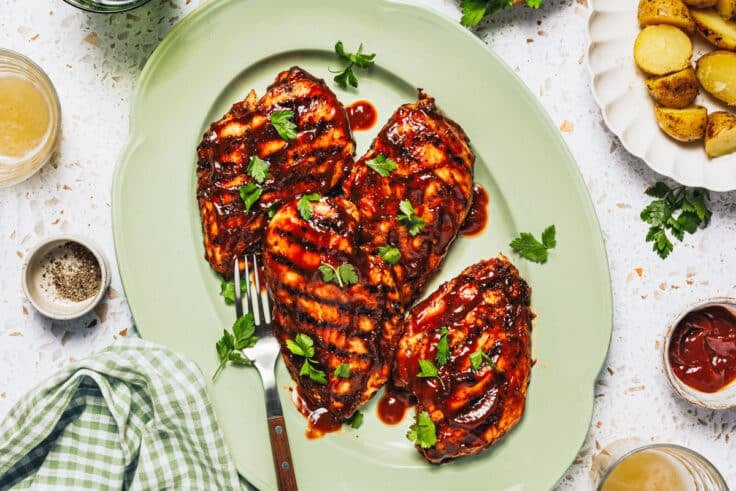 Horizontal overhead shot of grilled bbq chicken breast on a green serving tray.