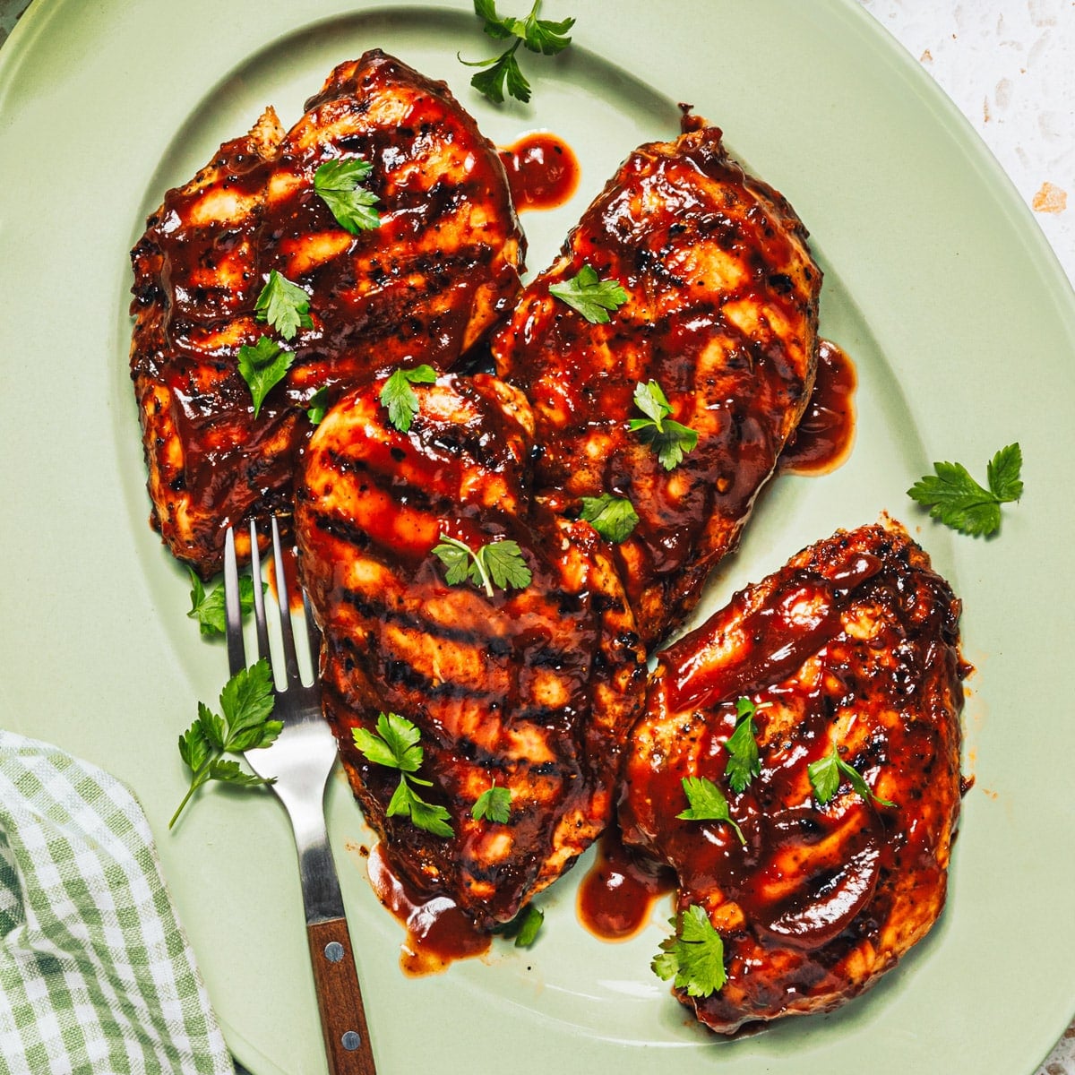 Square overhead image of grilled bbq chicken breast on a green serving tray.