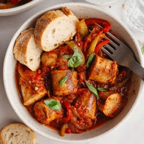 Square overhead shot of a bowl of Italian sausage and peppers with a side of crusty bread.