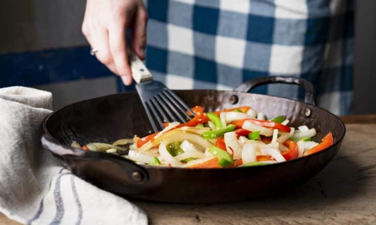 Stirring bell peppers and onions in a cast iron skillet.