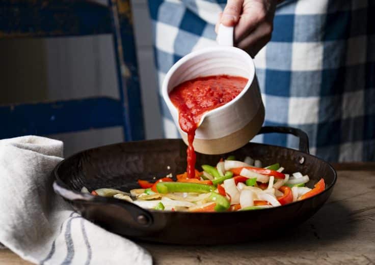 Pouring crushed tomatoes into a cast iron skillet.