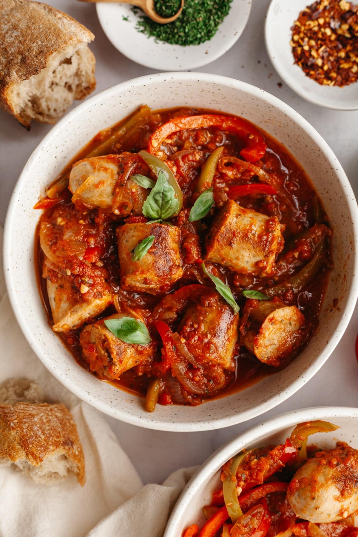 Overhead shot of a bowl of Italian sausage and peppers with a side of crusty bread.