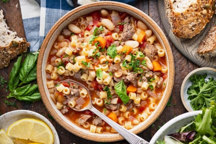 Horizontal overhead image of a bowl of pasta fagioli soup on a rustic wooden table.