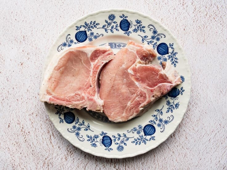 Patting brined pork chops dry on a blue and white plate.