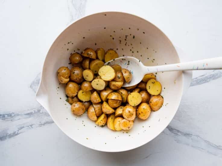 Tossing together potatoes with olive oil and seasoning in a mixing bowl.