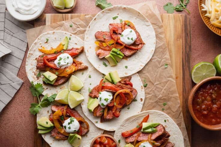 Horizontal overhead image of tortillas topped with sheet pan steak fajitas ingredients.