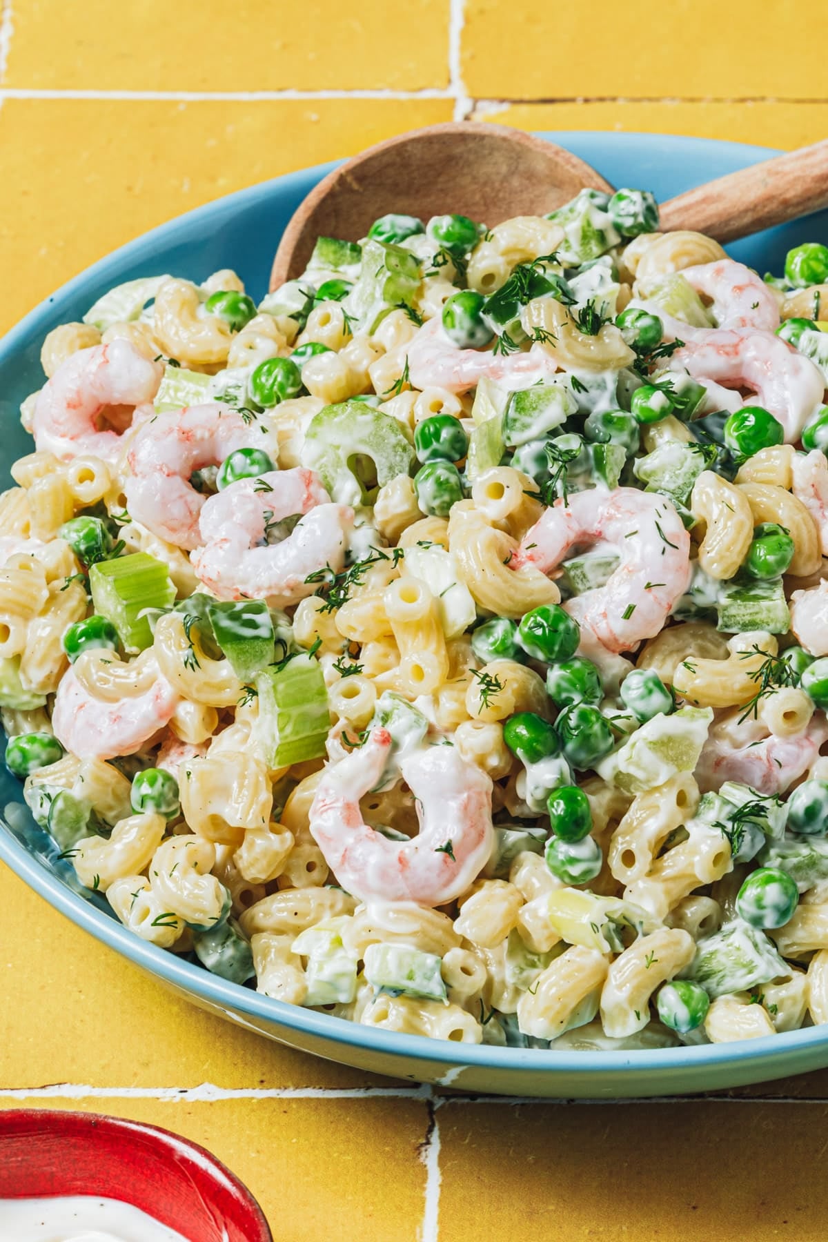 Close up side shot of shrimp pasta salad in a turquoise bowl on a yellow table.