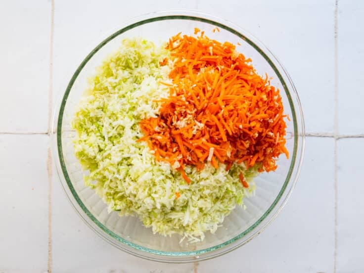 Shredded cabbage and carrots in a large glass bowl.