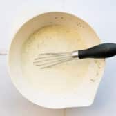 Whisking together a homemade coleslaw dressing in a white bowl.