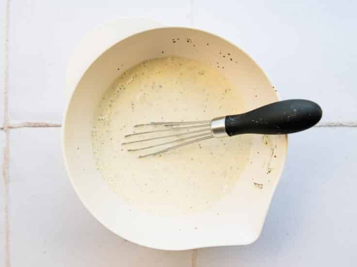 Whisking together a homemade coleslaw dressing in a white bowl.