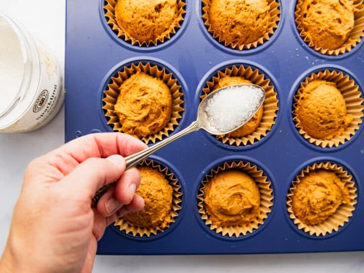 Sprinkling coarse sugar over the top of pumpkin muffin batter.