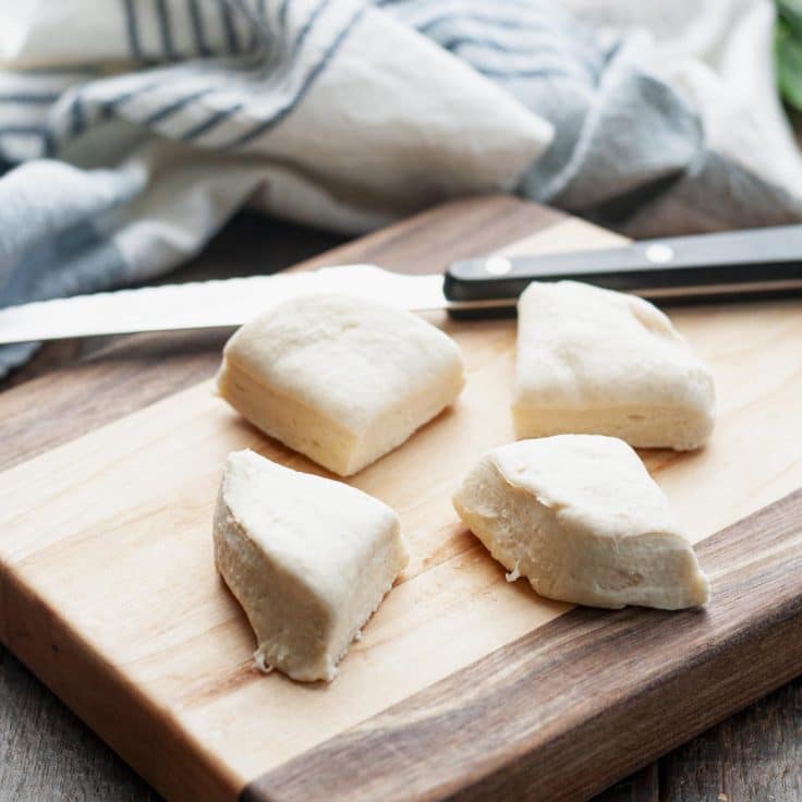 Cutting canned biscuit dough into quarters on a wooden cutting board.