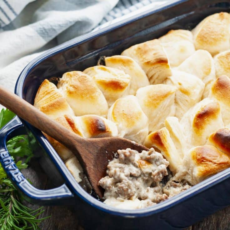 Square side shot of breakfast casserole with biscuits and gravy in a blue baking dish.