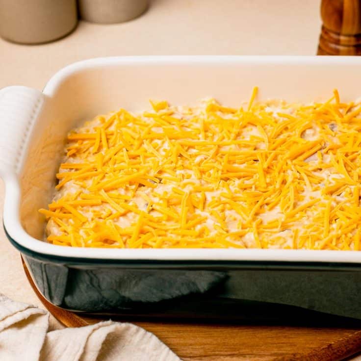 Adding the cheese on top of a chicken tater tot casserole.