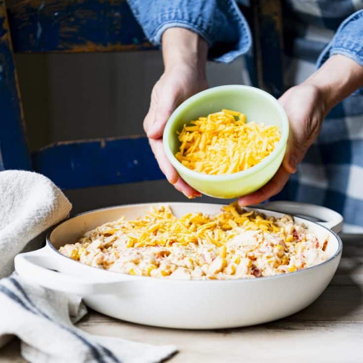 Adding cheese to the top of a chicken Dorito casserole.