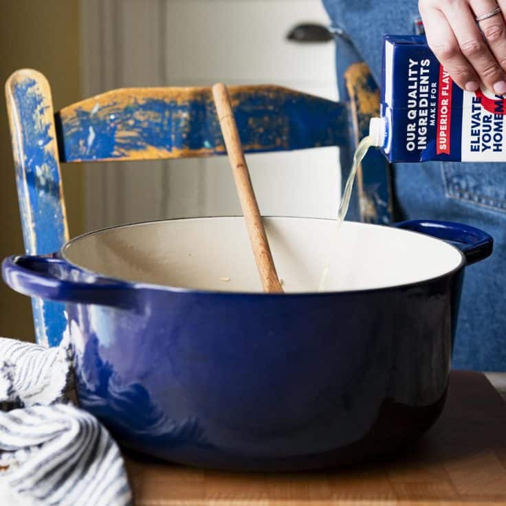 Pouring chicken broth into a Dutch oven.
