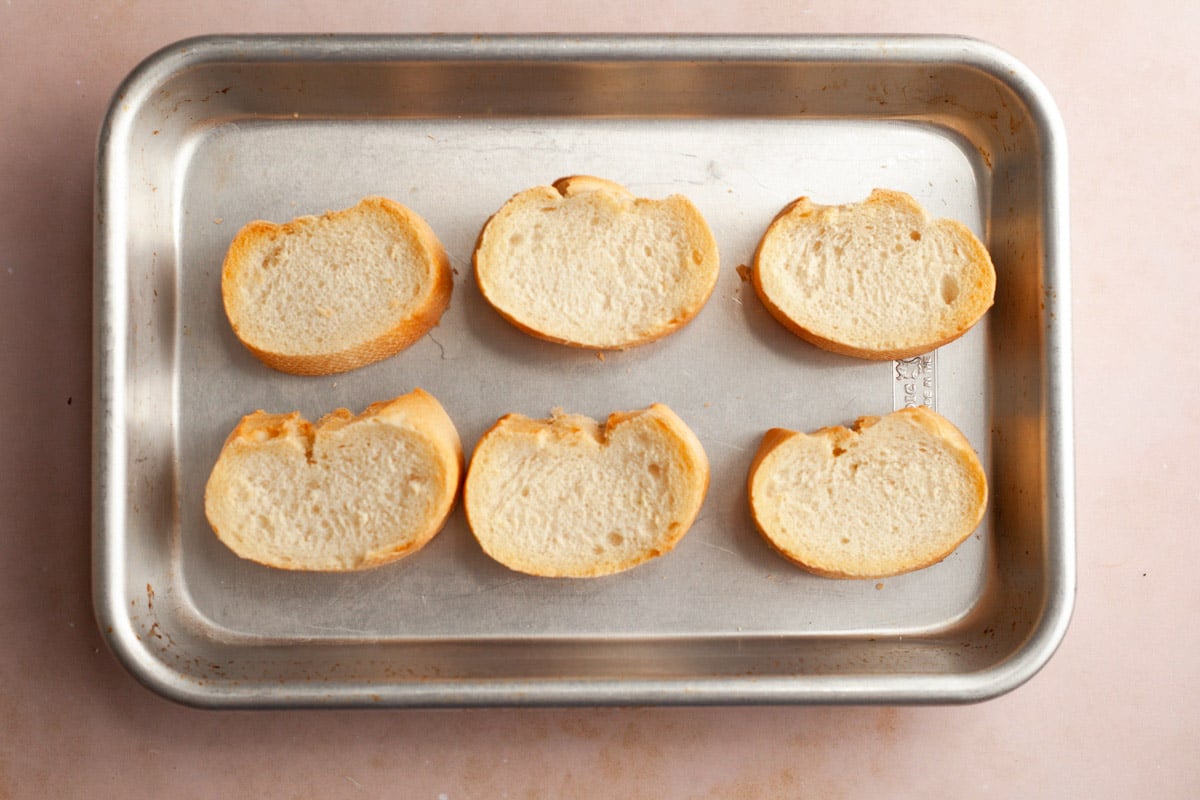 Toasted slices of baguette on a baking sheet.