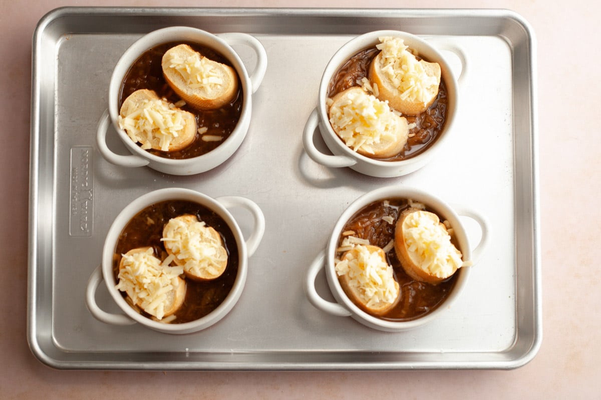 Arranging bread and cheese on top of the bowls of soup.