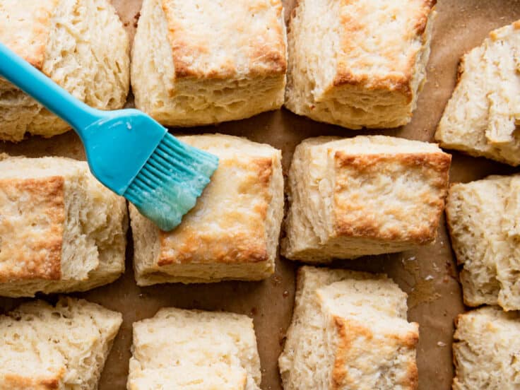 Brushing melted butter on the tops of the baked biscuits.