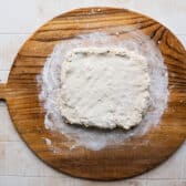 Biscuit dough flattened into a rectangular on a wooden board.