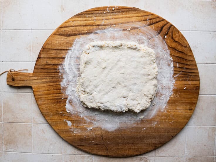Biscuit dough flattened into a rectangular on a wooden board.