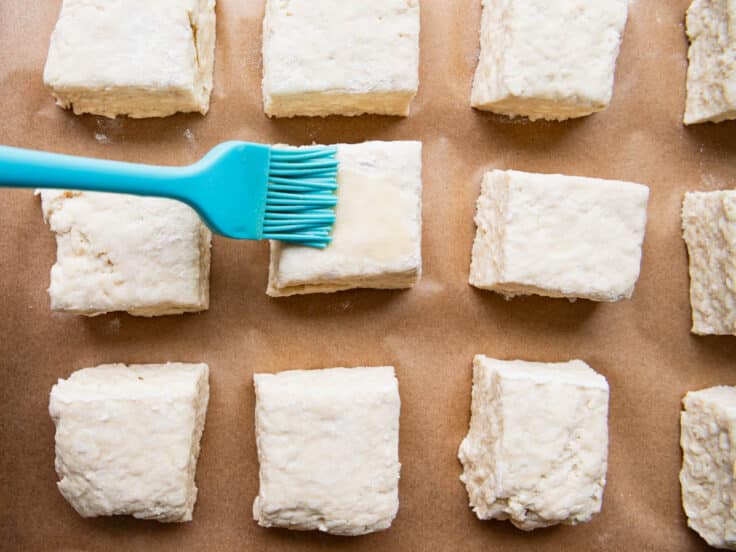 Brushing melted butter on biscuits before they go in the oven.