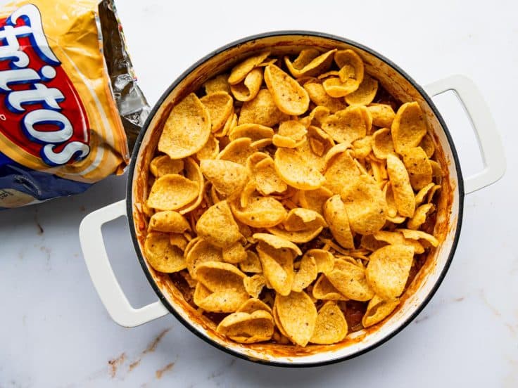 Adding cheese and Fritos to the top of a Frito pie recipe before baking.