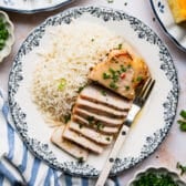 Square overhead shot of a sliced oven baked pork chop on a dinner plate with a side of rice.