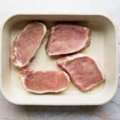 Pork chops in a white baking dish.