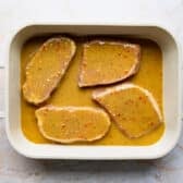 Four pork chops in a baking dish with sauce before going in the oven.