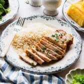Horizontal side shot of a sliced oven baked pork chop on a dinner plate with a side of rice.