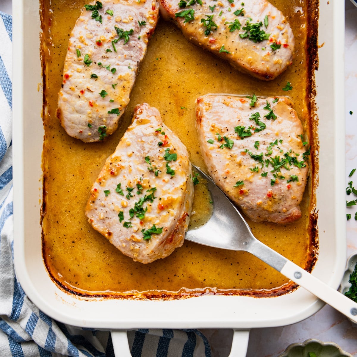 Square overhead shot of baked pork chops in a white dish.