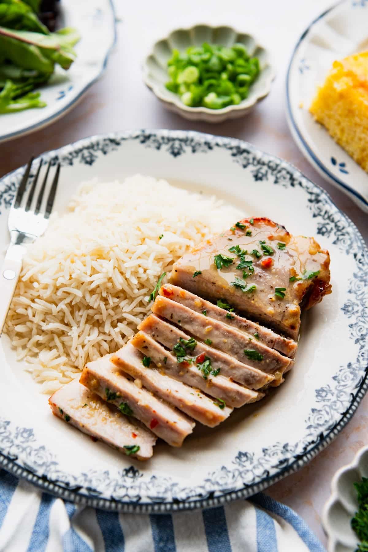 Side shot of a sliced oven baked pork chop on a dinner plate with a side of rice.