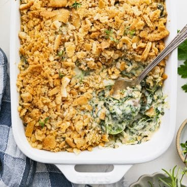 Square overhead shot of a serving spoon in a dish of the best creamed spinach casserole recipe.