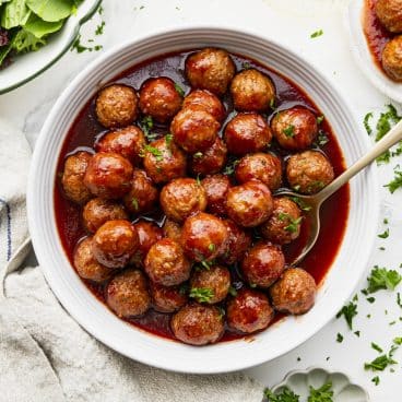Square overhead shot of Crock Pot meatballs in a white bowl with fresh parsley garnish.