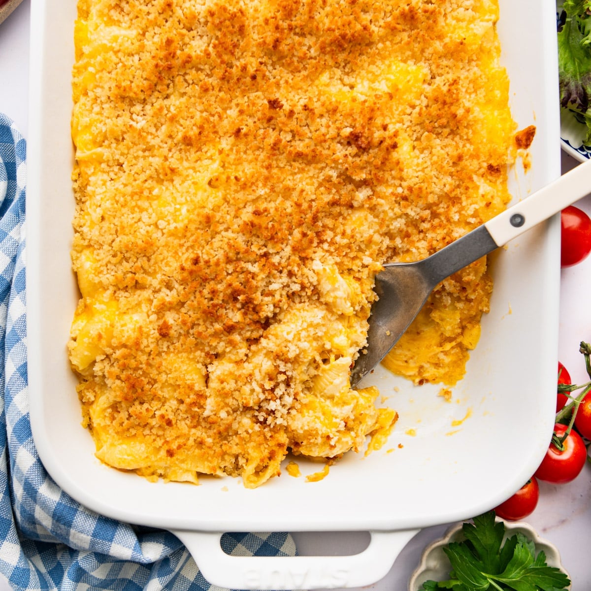 Square overhead shot of a serving spoon in a white baking dish full of homemade mac and cheese with sour cream and mayo.