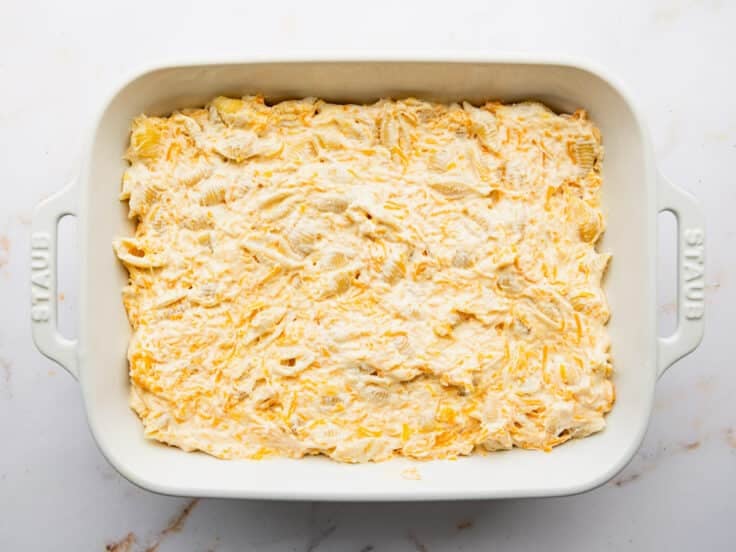Spreading the cheese and pasta mixture in a white baking dish.