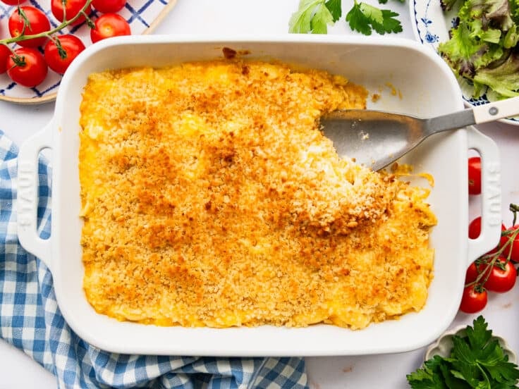 Horizontal overhead shot of a serving spoon in a white baking dish full of homemade mac and cheese with sour cream and mayo.