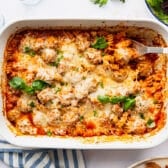 Horizontal overhead image of a baked meatball casserole garnished with fresh basil.