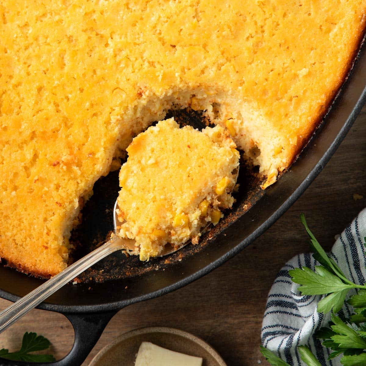 Square overhead shot of a spoon in a pan of Jiffy corn pudding.