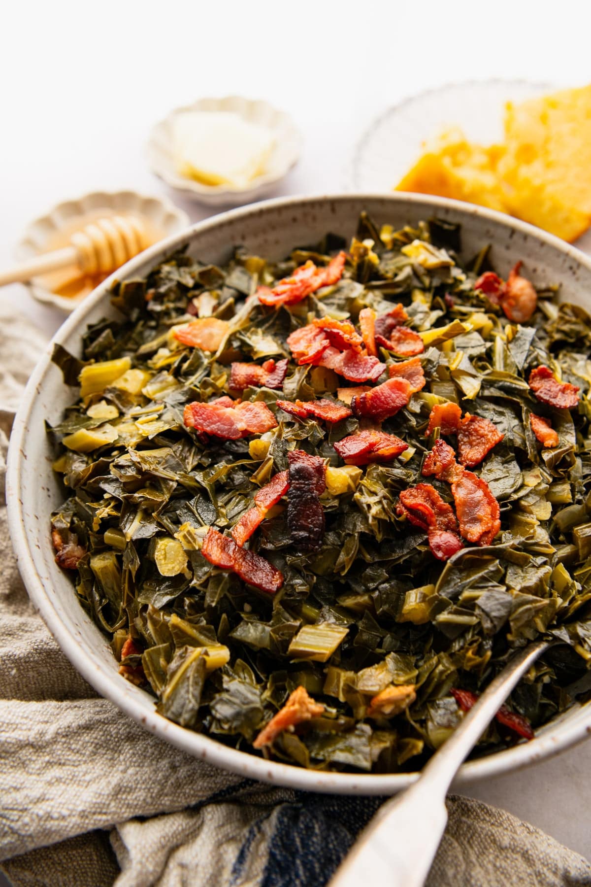 Close up side shot of Southern collard greens in a serving bowl with crispy bacon on top for garnish.